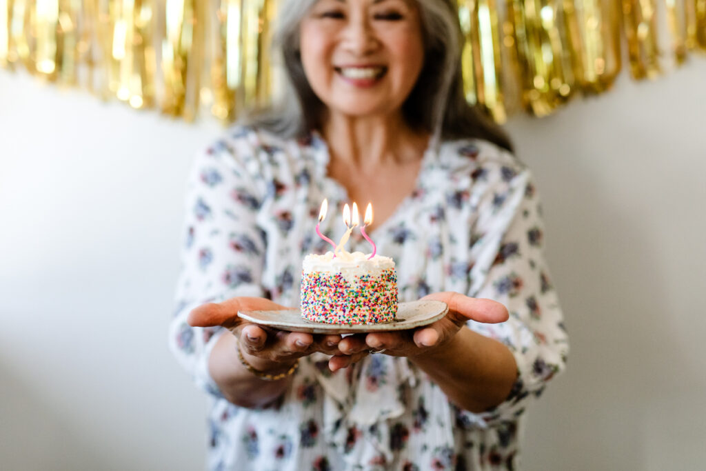 Smiling senior woman holding birthday cake with burning candles. 