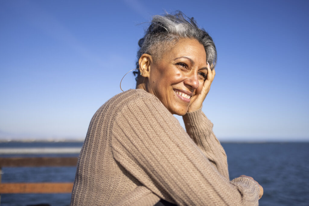 A mature woman relaxes on the pier at the beach on a cool day in a sweater.