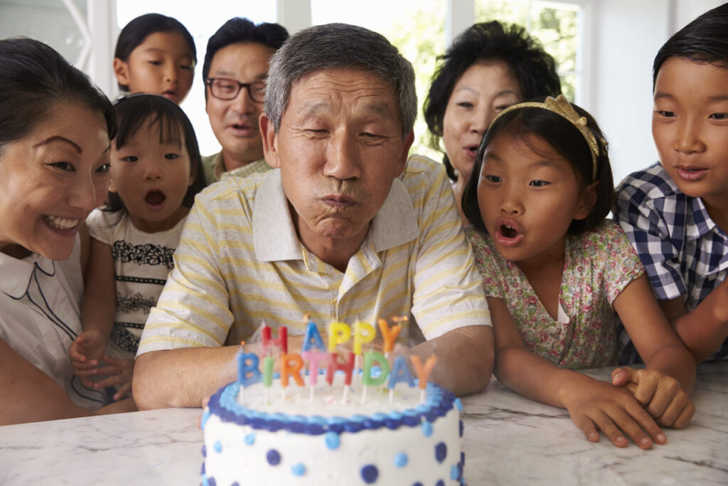 Grandfather Blows Out Candles On Birthday Cake