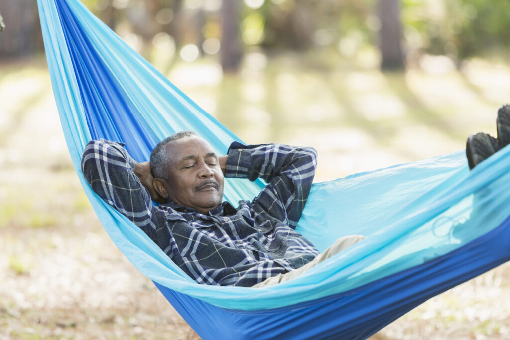 A senior man sound asleep in a hammock in the park. 