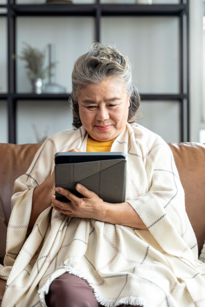 senior woman with plaid shawl sitting on couch using tablet
