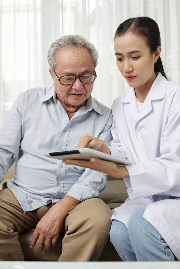 Female doctor in white coat sitting with senior patient and reviewing information on a tablet