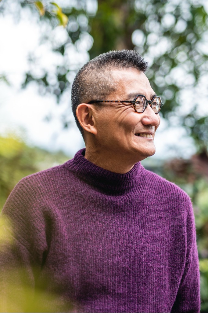 Senior man with purple sweater in front of trees.