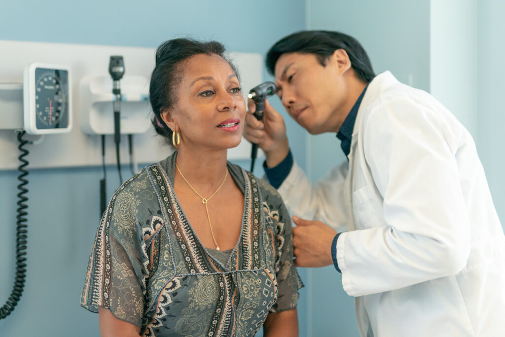 A senior woman is at a routine medoctor is checking a senior patient's ears after reporting changes in her hearing recently.