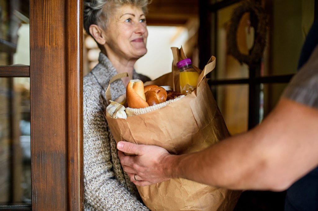 Senior woman smiles receiving a grocery delivery at her front door.