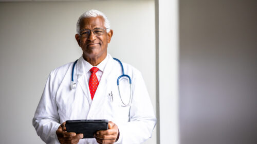 A senior black doctor with a tablet with window lighting.