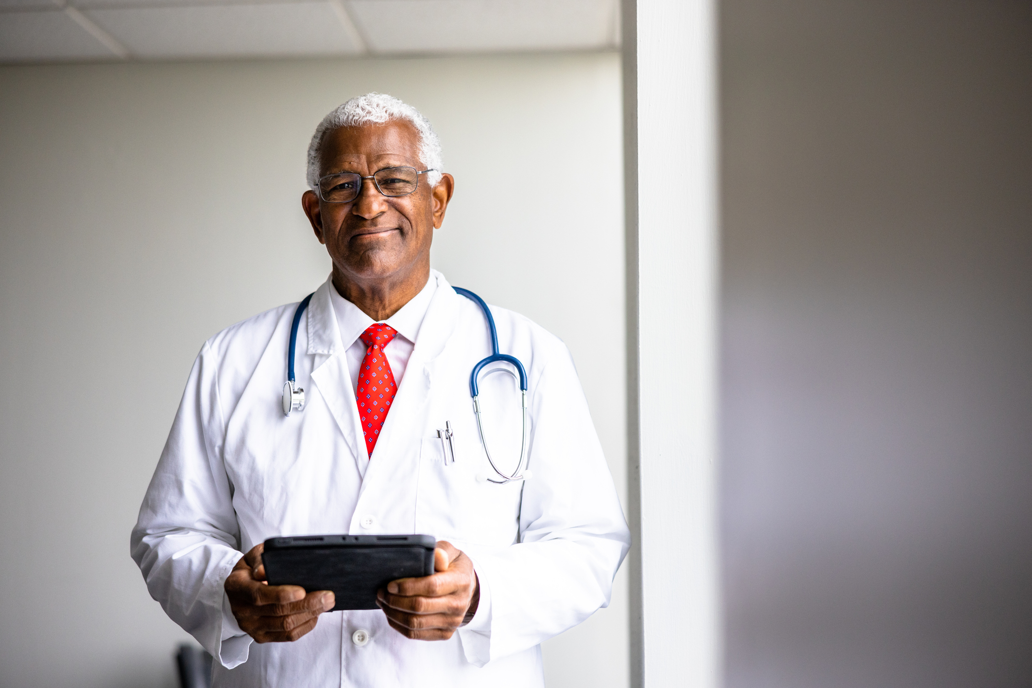 A senior black doctor with a tablet with window lighting.